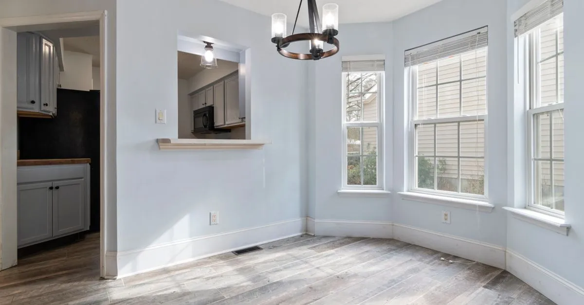 Sunlit empty room featuring a modern chandelier and wooden floors, ideal for home staging.